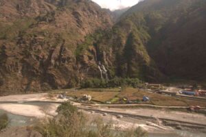Waterfall cascading down cliffs above a riverside village on the Annapurna Circuit Trek route