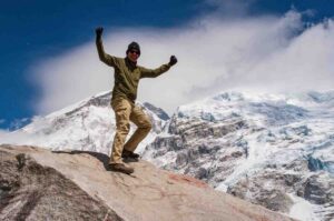Trekker celebrating on a rock with glacier peaks in the background on the Everest Base Camp Trek