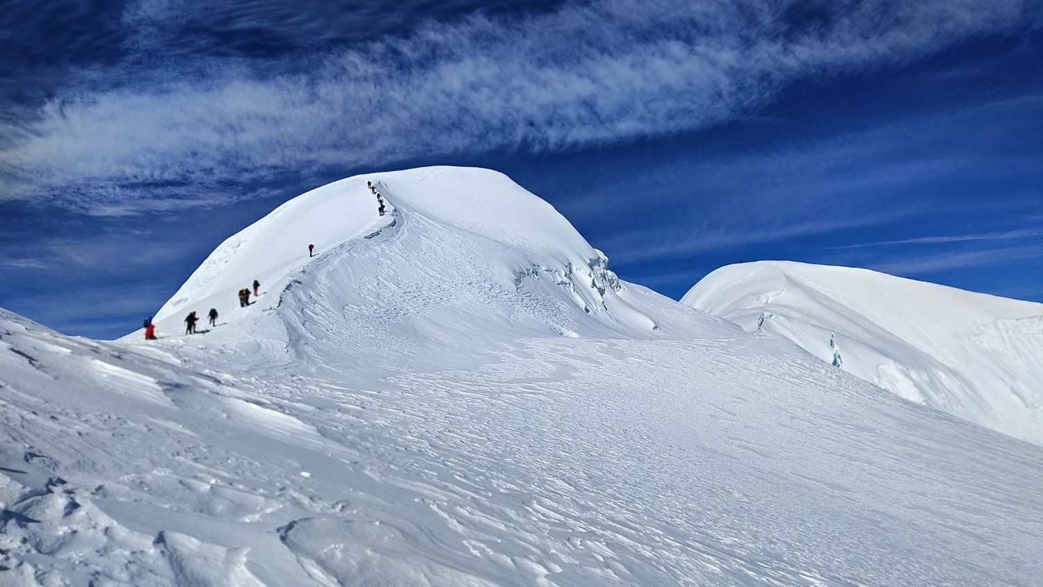Climbers approaching a snowy summit ridge